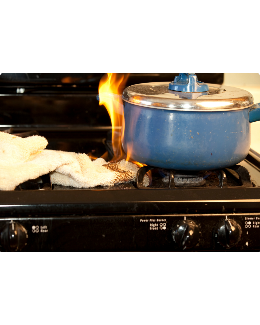 A blue pot sitting on a stove with a white towel catching fire from the burner.